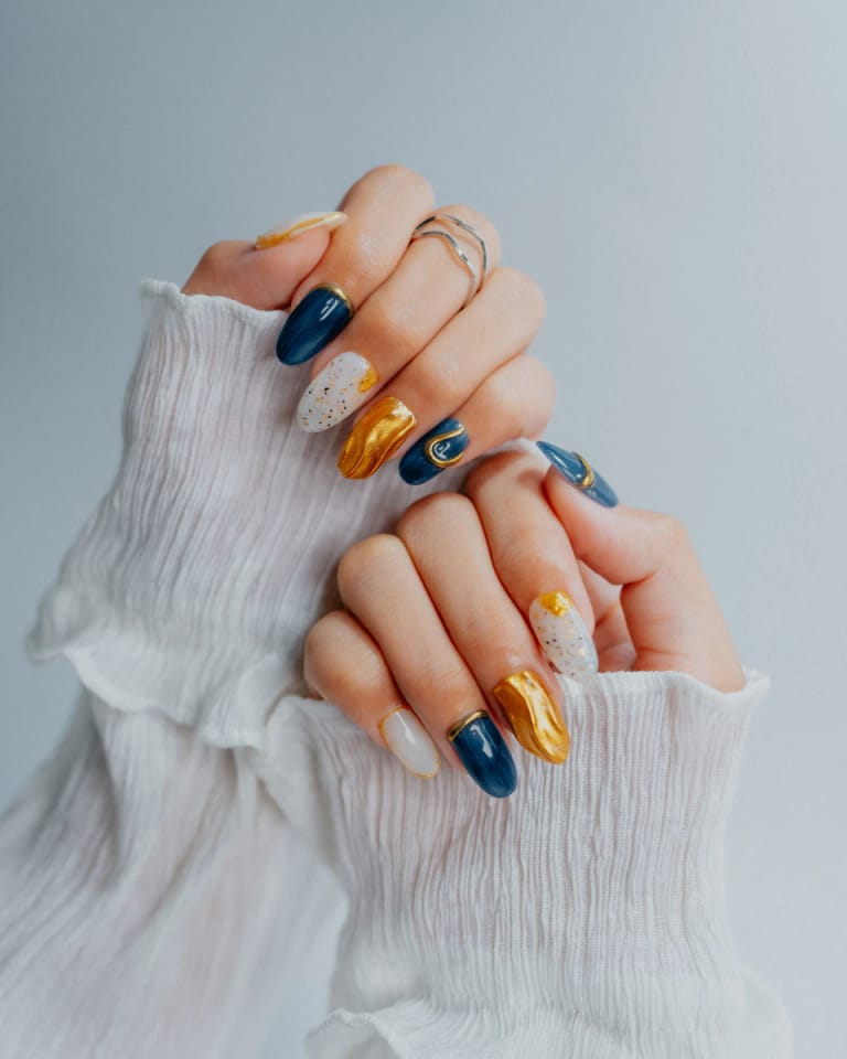 Nail art ornamentado en azul marino, dorado y blanco sobre tejido de gasa