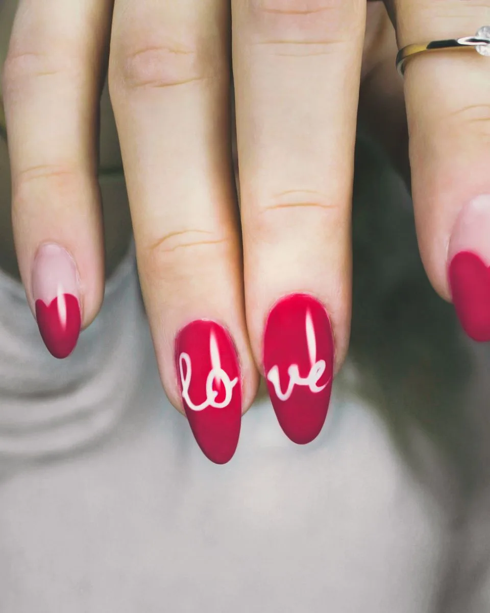 Uñas almendra en rojo intenso con la palabra love trazada a mano