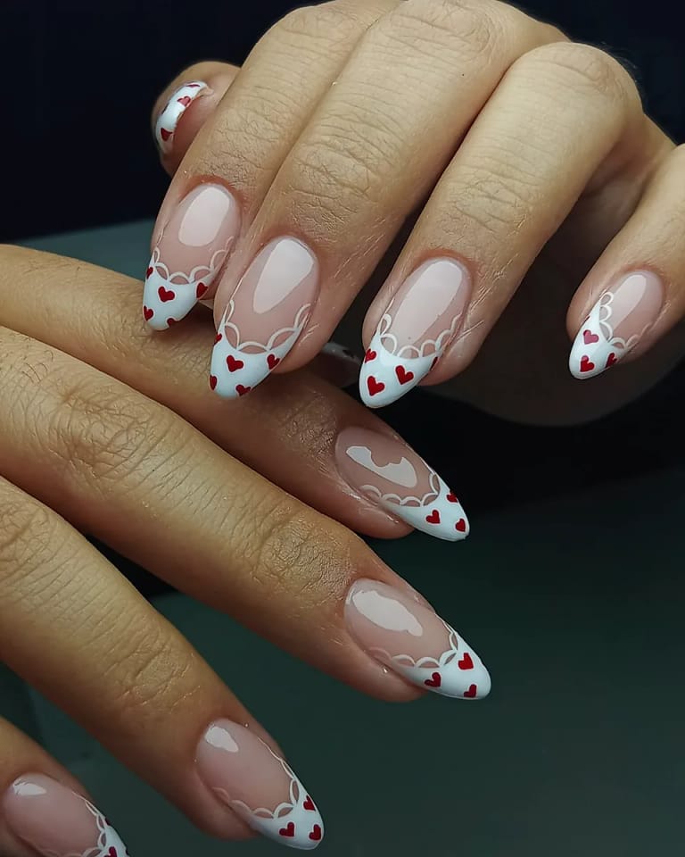 Uñas almendra nude con corazones rojos y blancos pintados a mano